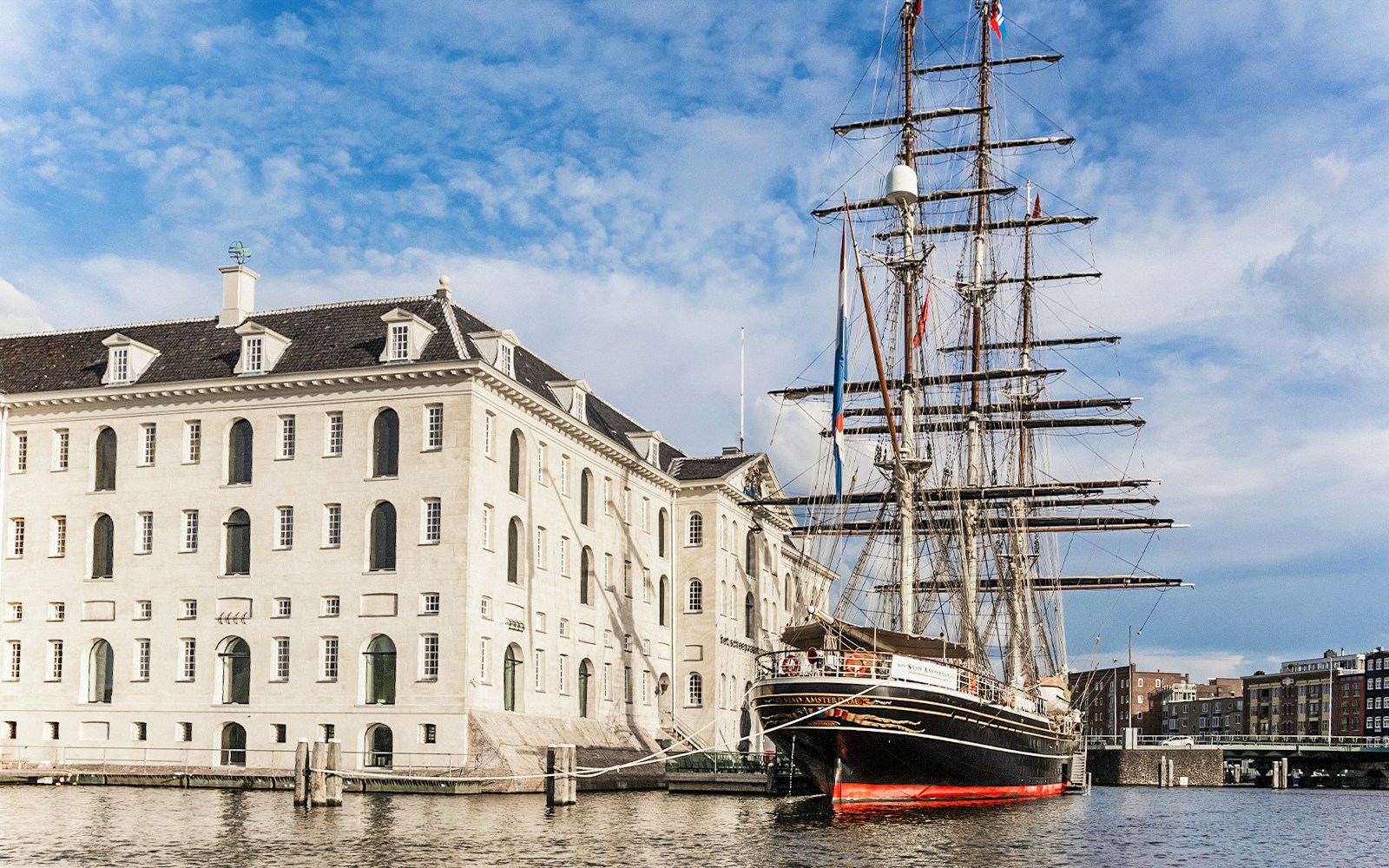 National Maritime Museum in Amsterdam with historic ship docked nearby.