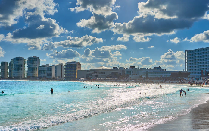 Beachfront view of Mandala Beachclub Cancun with people enjoying the ocean.