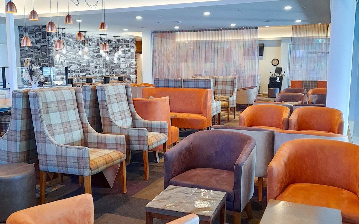 Plaza Premium Lounge seating area with plaid and orange chairs, modern lighting, and a photo wall.