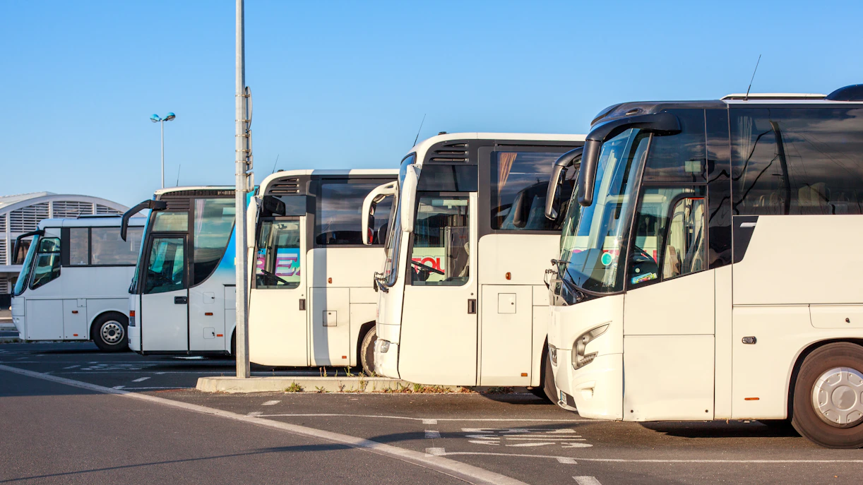 Buses parked at a station with a modern terminal building in the background.