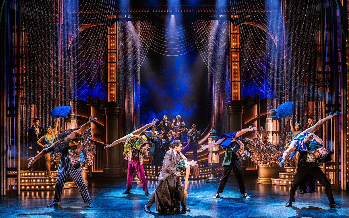 Dancers performing a lively scene from The Great Gatsby musical with vibrant costumes and art deco set.