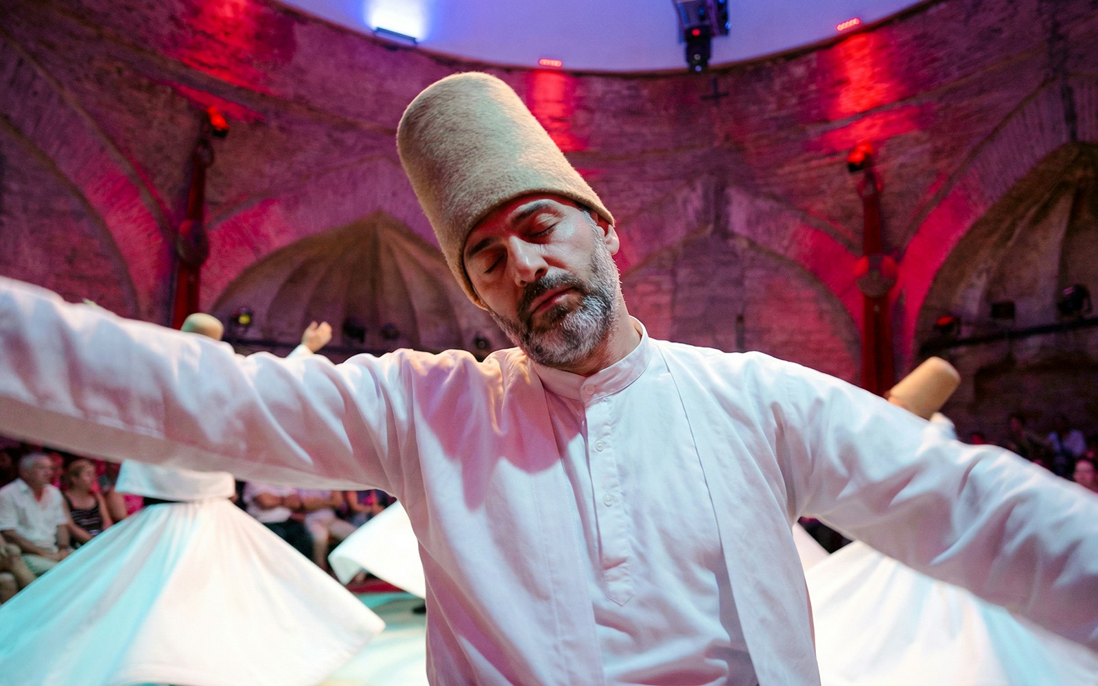 Whirling Dervishes performing in a historic venue with an audience in Istanbul.