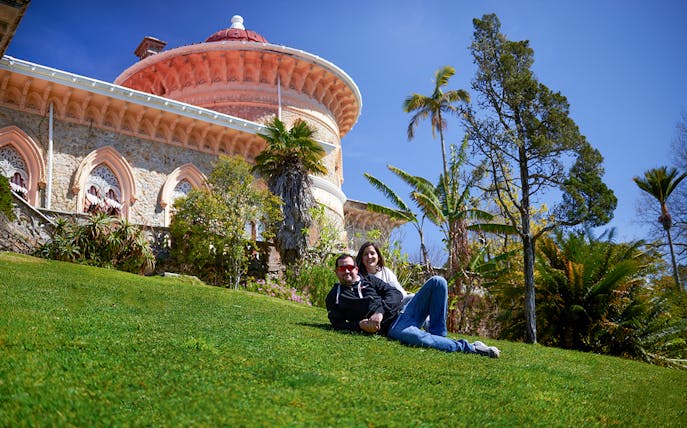Couple relaxing on grass in front of Monserrate Palace, Sintra, Portugal.