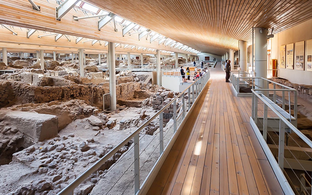 Visitors walking along a wooden walkway inside Akrotiri Excavations, Santorini.