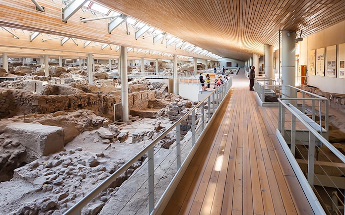 Visitors walking along a wooden walkway inside Akrotiri Excavations, Santorini.