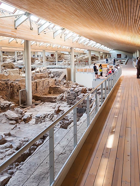Visitors walking along a wooden walkway inside Akrotiri Excavations, Santorini.