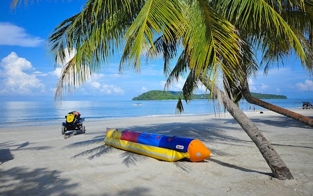 Banana boat on sandy beach under palm trees at Paradise 101, with island view in the background.