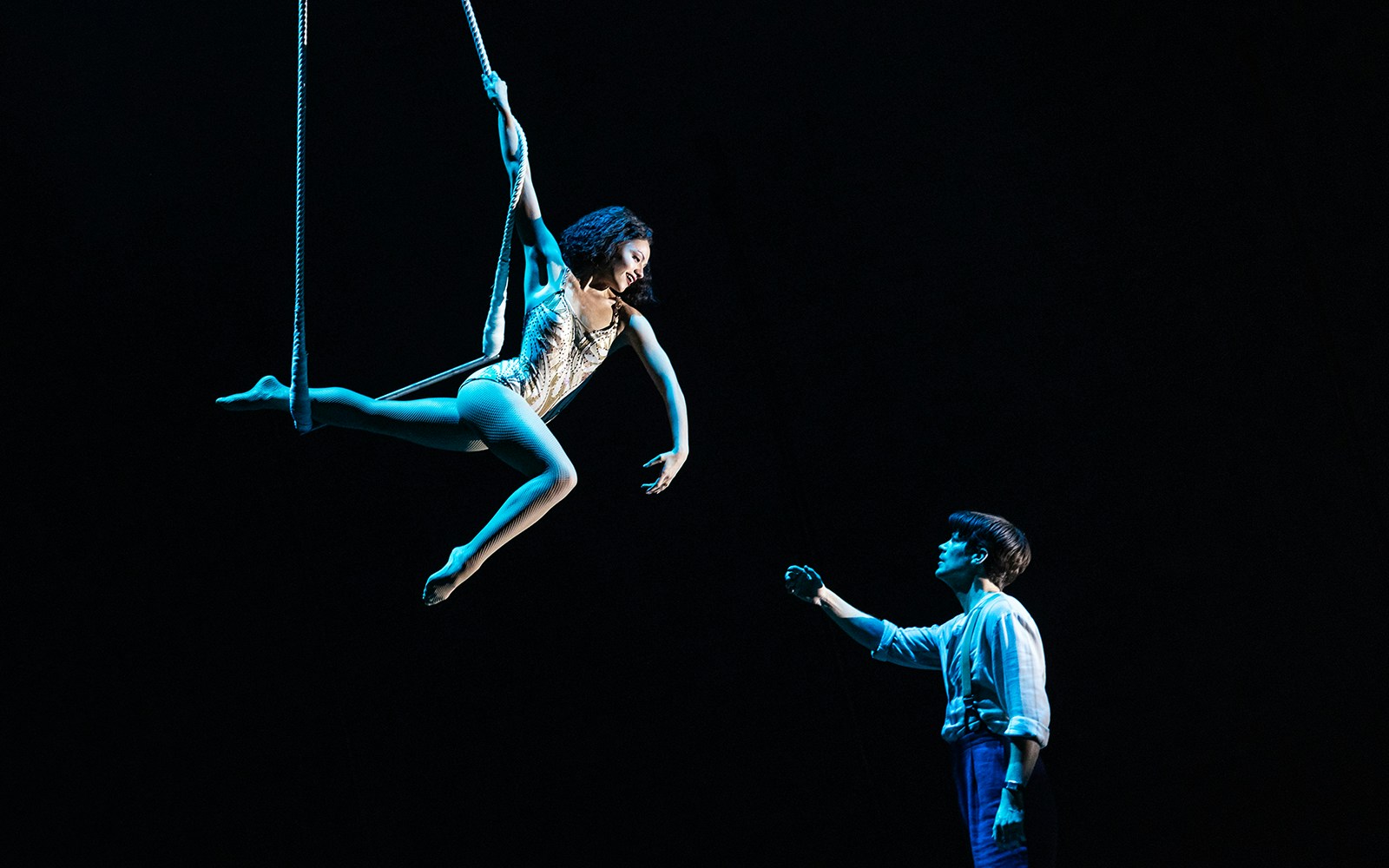 Aerial performer on trapeze with a person reaching up, "Water for Elephants" show.