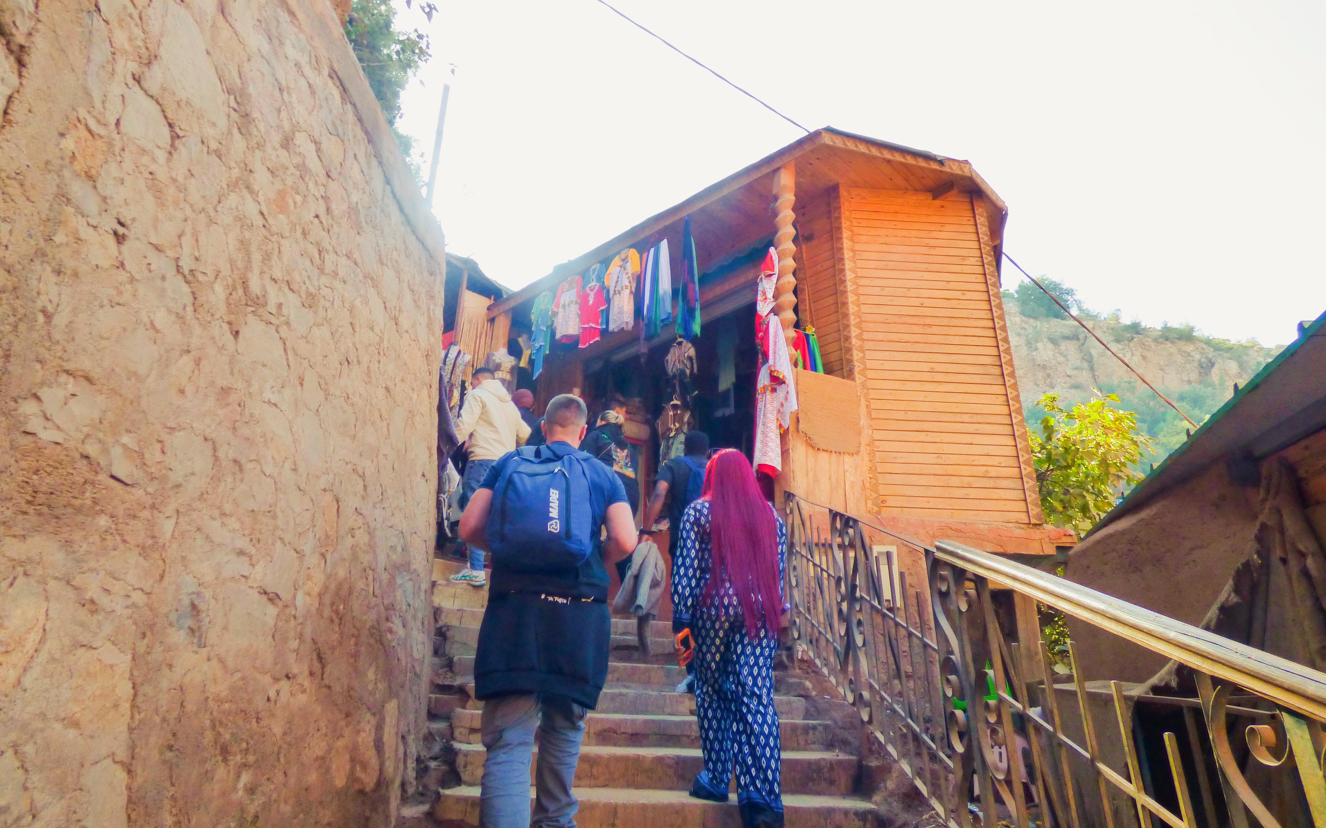 Tourists hiking to Ouzoud Waterfalls, passing local shops with colorful garments.