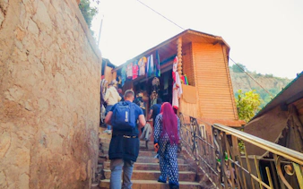 Tourists hiking to Ouzoud Waterfalls, passing local shops with colorful garments.
