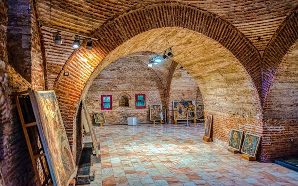 Art gallery inside Mogosoaia Palace, Romania, featuring brick arches and paintings on display.