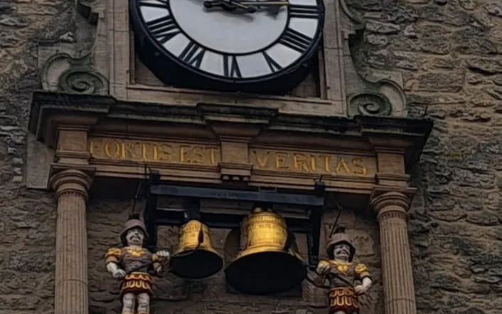 Oxford clock tower with Latin inscription and figures, part of self-guided city exploration game.