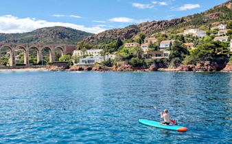 Paddleboarder on Villefranche bay with coastal homes and viaduct in background.