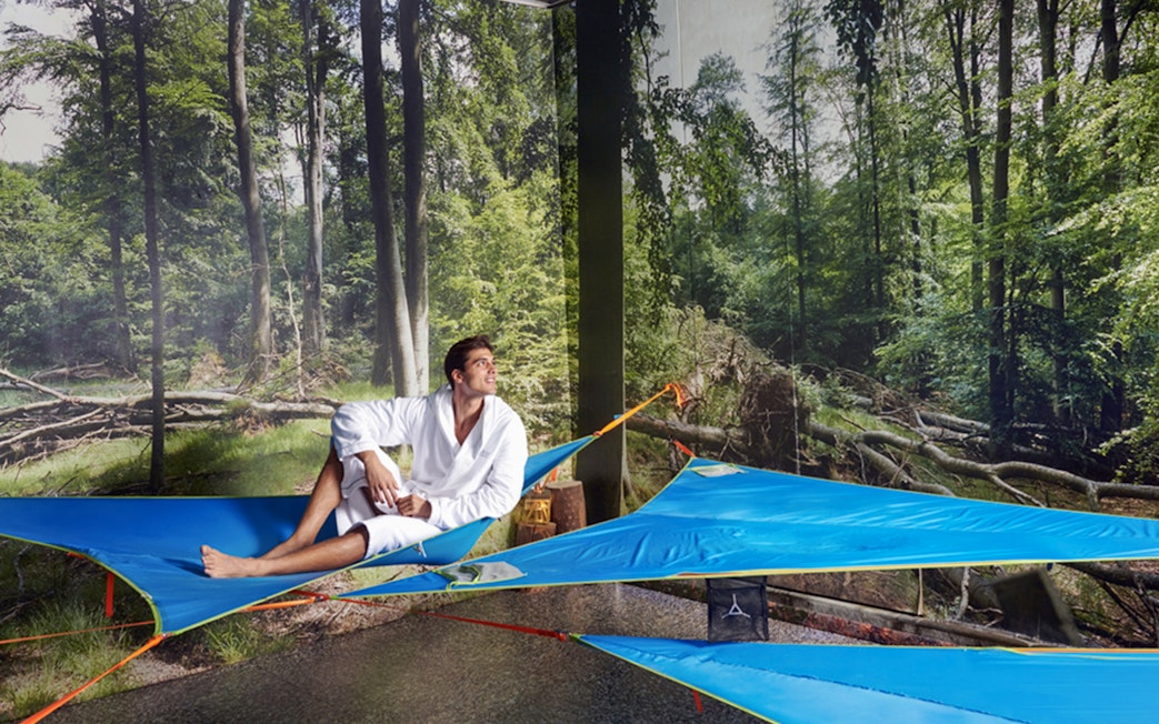 Man relaxing on a blue hammock at QC Terme Pré Saint Didier spa with forest backdrop.