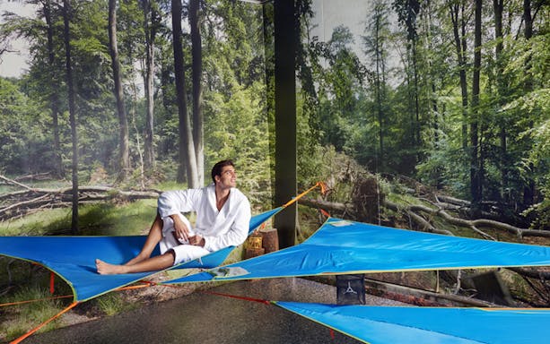 Man relaxing on a blue hammock at QC Terme Pré Saint Didier spa with forest backdrop.