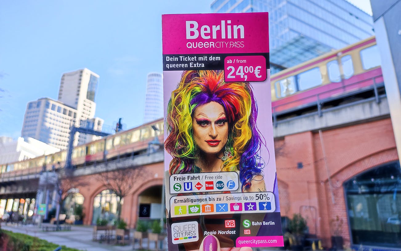 QueerCityPass Berlin ABC flyer with colorful drag performer, cityscape background.