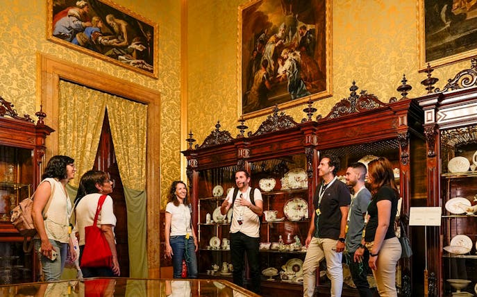 Tour group exploring the Royal Palace of Madrid's ornate room with guide.