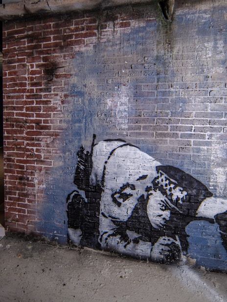 Street art on brick wall at Banksy Museum, Amsterdam, featuring a crouching figure.
