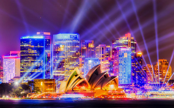 Sydney Opera House illuminated during Vivid Sydney festival with city skyline.