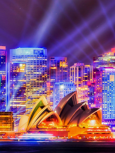 Sydney Opera House illuminated during Vivid Sydney festival with city skyline.
