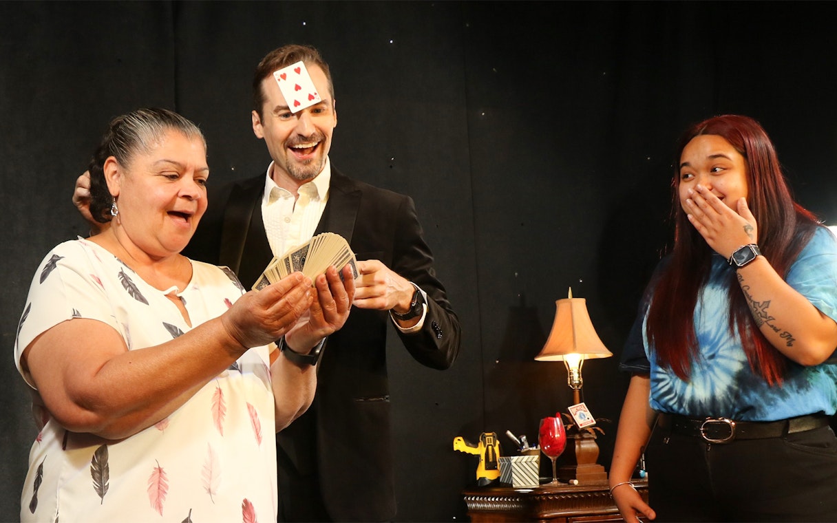 Magician performing card trick with audience members on stage.
