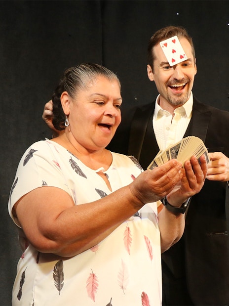 Magician performing card trick with audience members on stage.