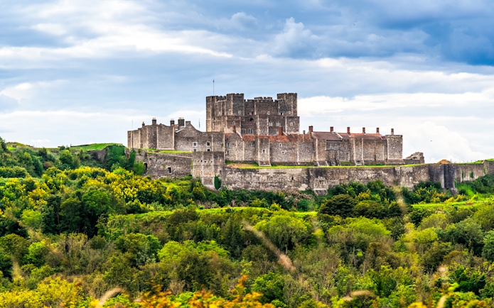 Dover Castle surrounded by lush greenery under a cloudy sky.