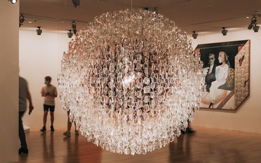 Exhibit at Alexander McQueen Mind, Mythos, Muse with intricate glass installation and visitors.