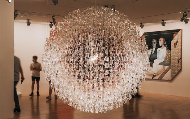 Exhibit at Alexander McQueen Mind, Mythos, Muse with intricate glass installation and visitors.