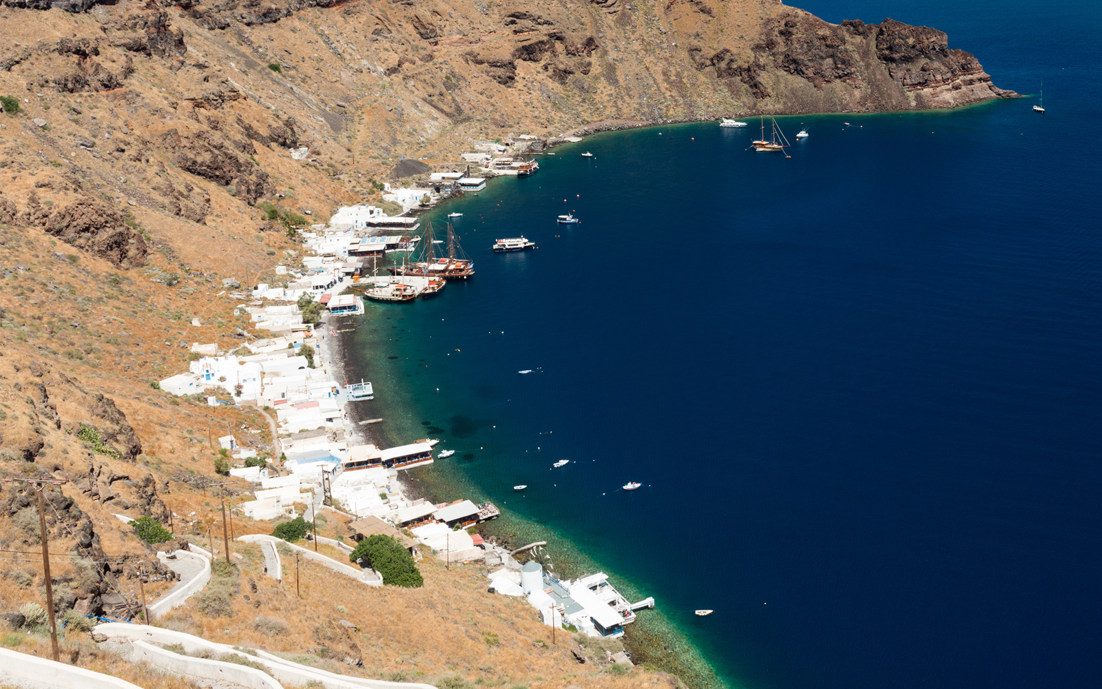 Aerial view of Manolas village coastline on Therasia island with boats in the bay.