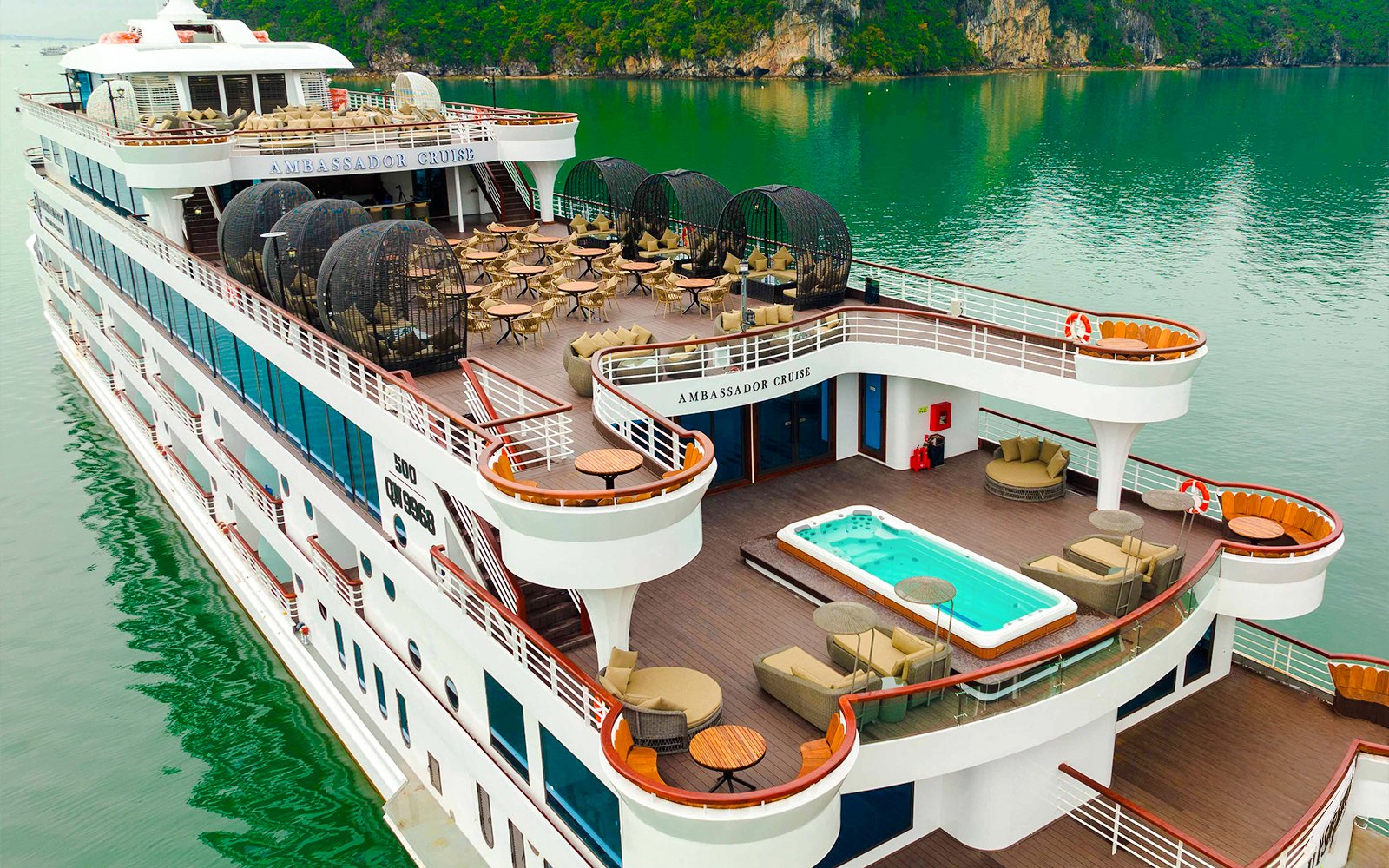 Aerial view of Ambassador cruise ship deck with seating and jacuzzi in scenic bay.