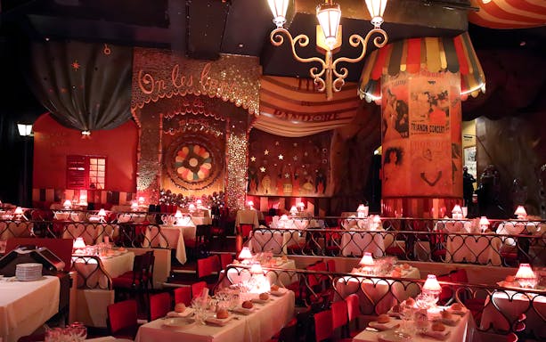 Moulin Rouge dining area with elegantly set tables and red lamps.