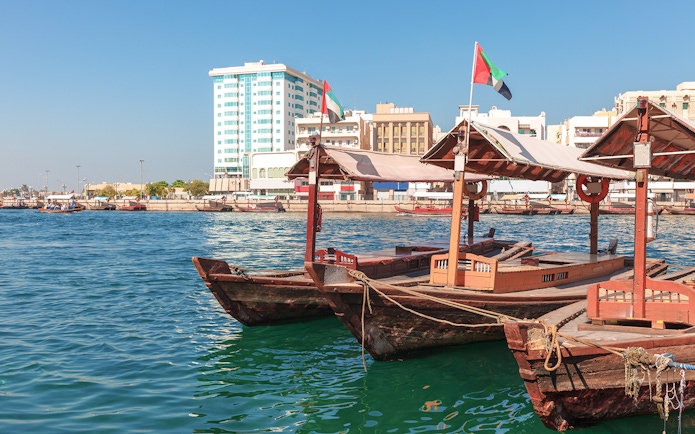 Traditional Abra boat docked at Dubai Creek pier with cityscape in the background.