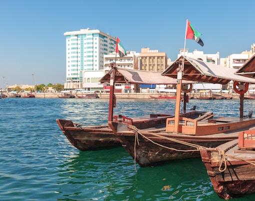 Traditional Abra boat docked at Dubai Creek pier with cityscape in the background.