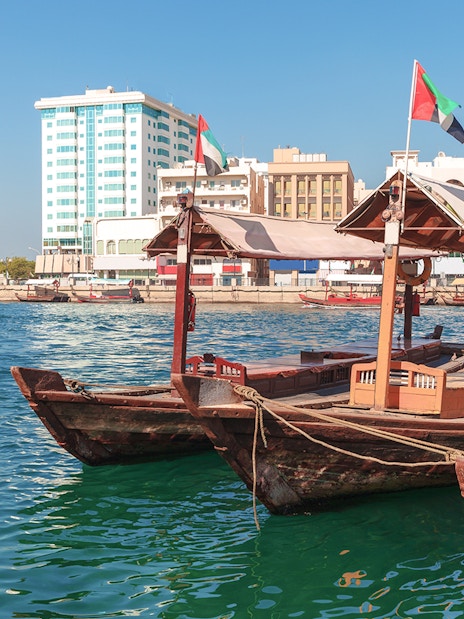 Traditional Abra boat docked at Dubai Creek pier with cityscape in the background.