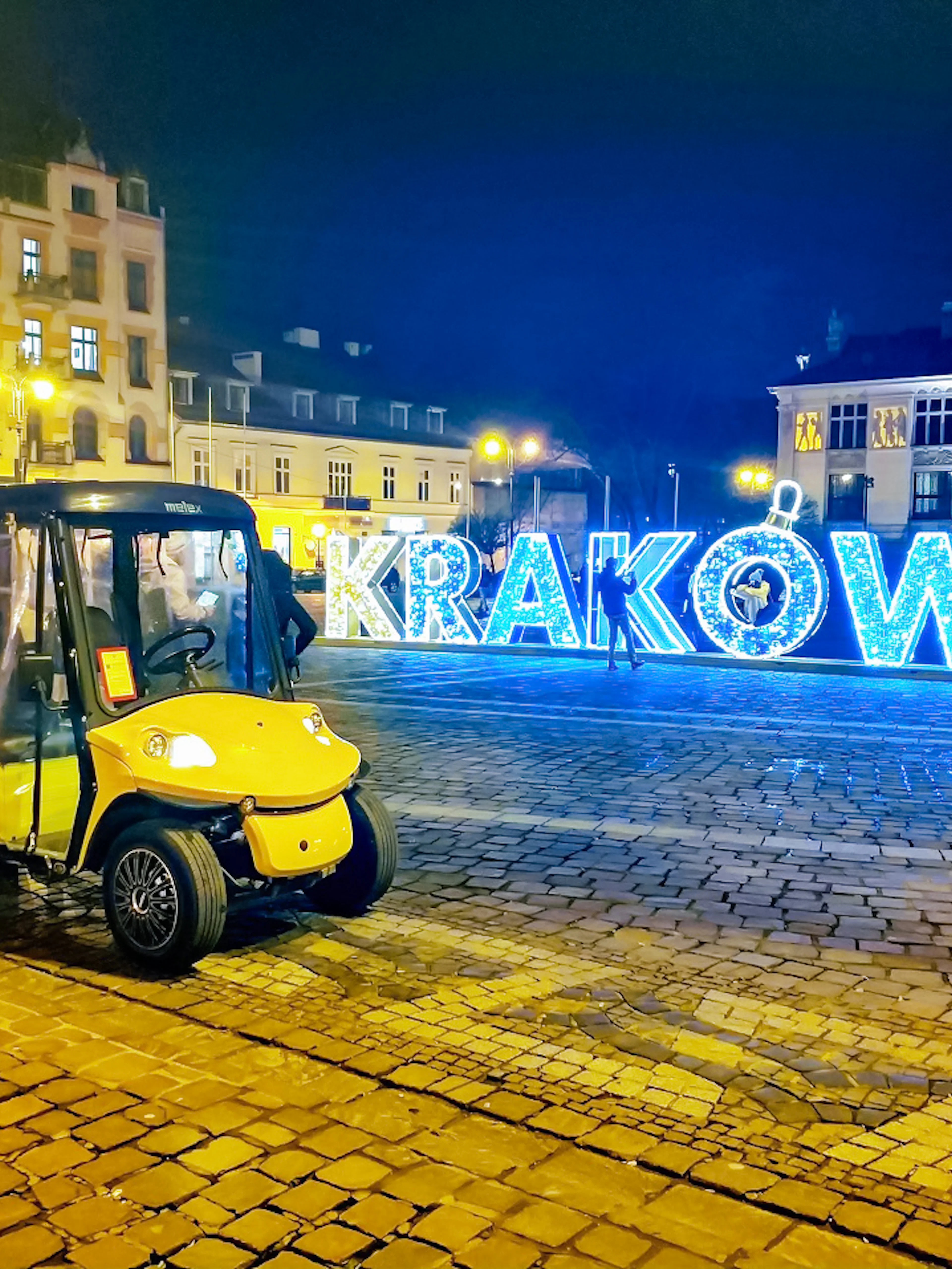 Golf cart in Krakow Old Town at night with illuminated sign.