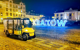 Golf cart in Krakow Old Town at night with illuminated sign.