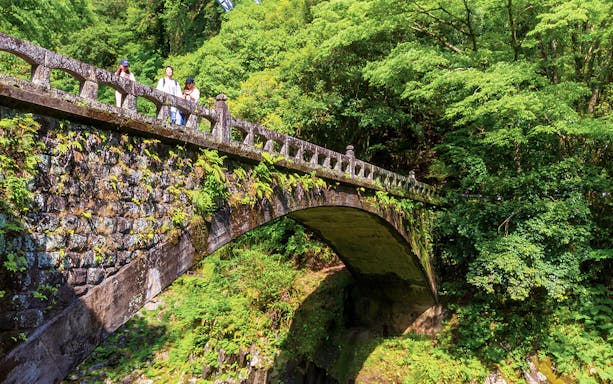 Visitors on a stone bridge surrounded by lush greenery in Takachiho, Miyazaki during a day tour from Fukuoka.