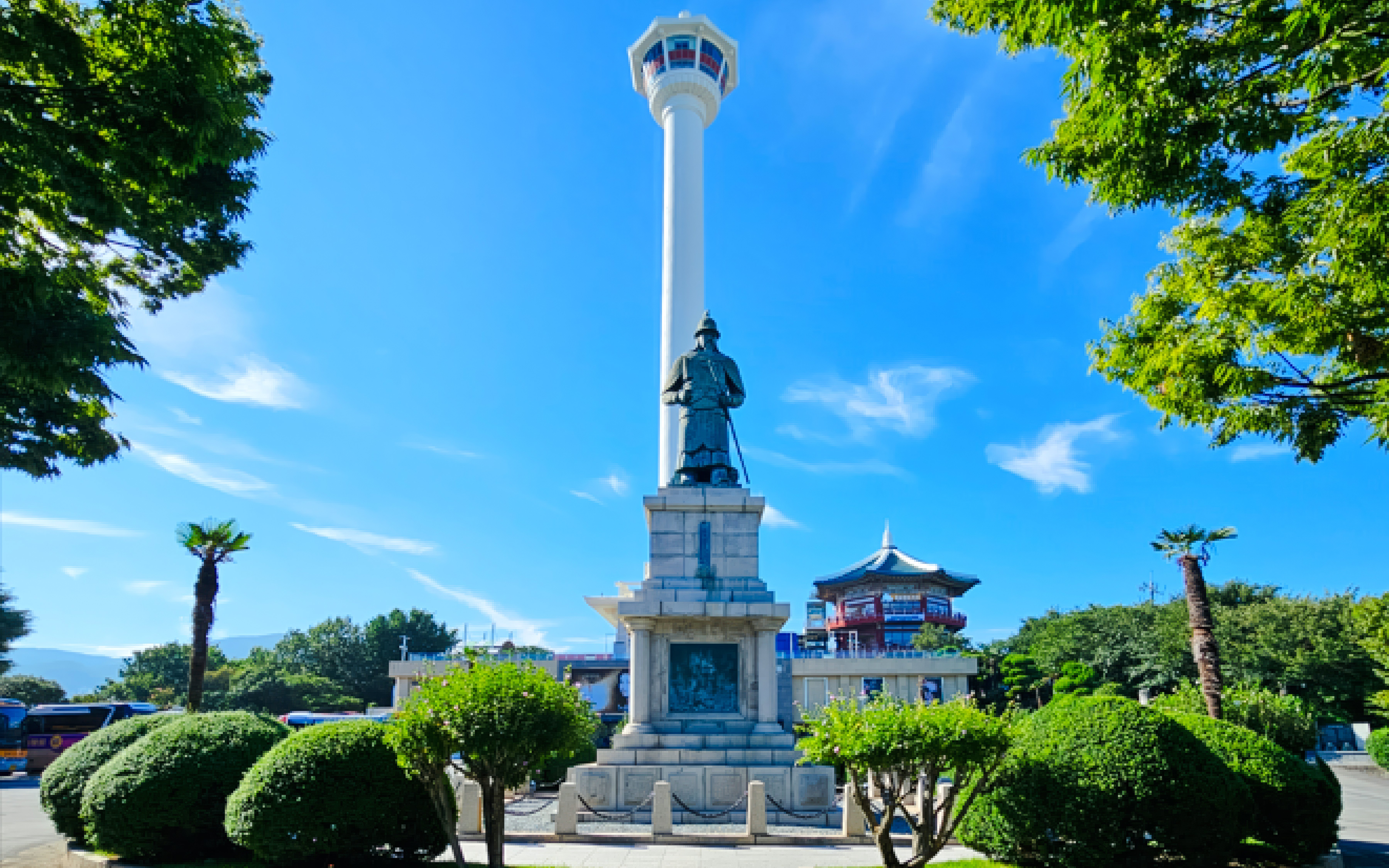 Busan Tower with statue and surrounding greenery under a clear blue sky.