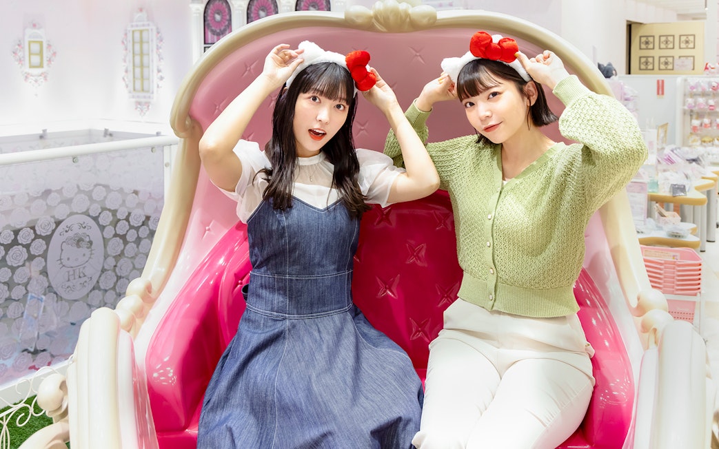 Visitors wearing Hello Kitty headbands at Sanrio Puroland, seated on a themed bench.