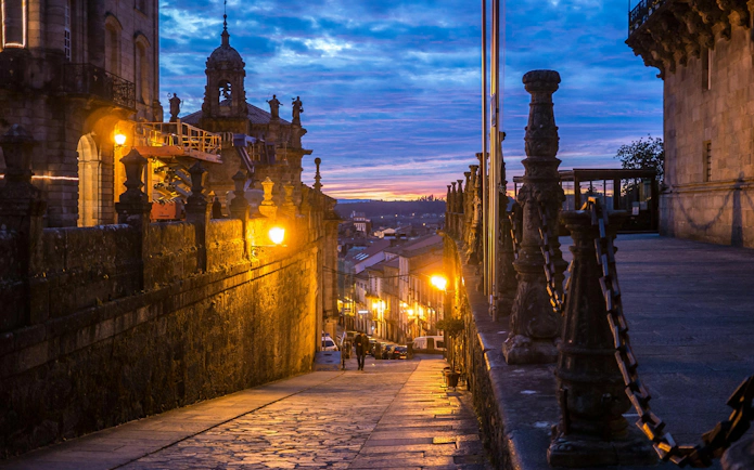 Street in Santiago de Compostela at dusk with historic buildings and vibrant Galician skies.