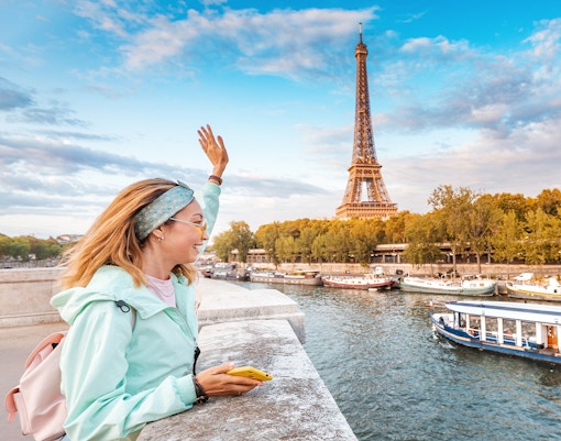 Tourist waving to a Seine river cruise near the Eiffel Tower in Paris.