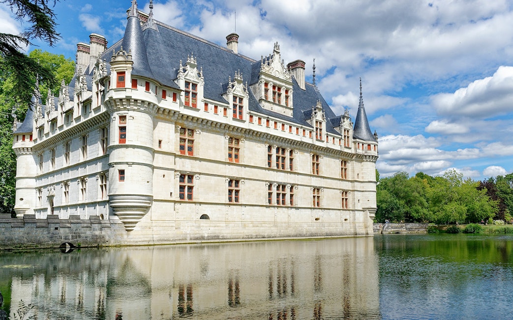Azay le Rideau Castle reflecting in a calm river under a blue sky.