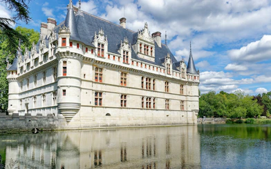 Azay le Rideau Castle reflecting in a calm river under a blue sky.
