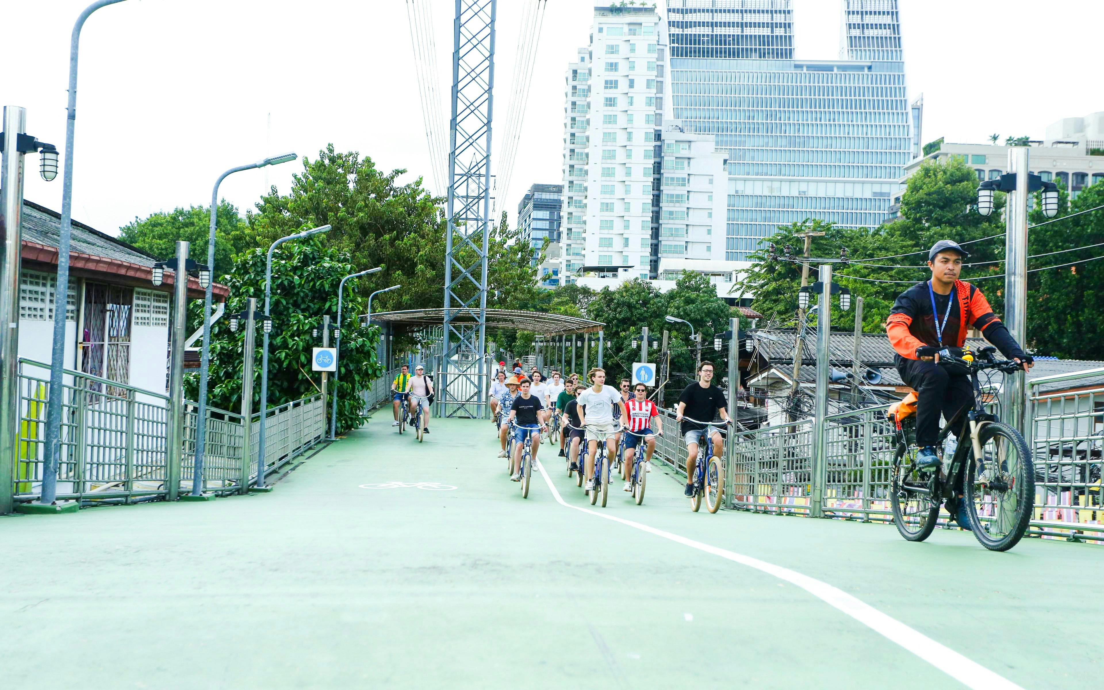 Tourists biking on a green path in Bangkok city with modern buildings in the background.
