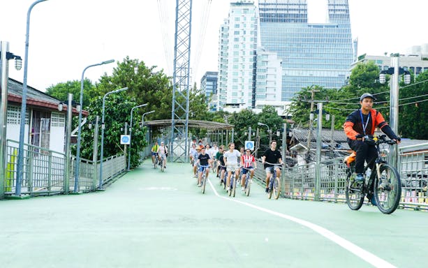 Tourists biking on a green path in Bangkok city with modern buildings in the background.