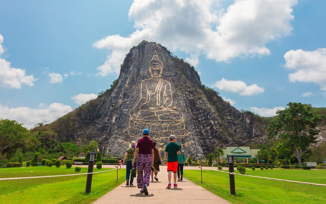 Visitors walking towards Buddha Mountain, Khao Chi Chan, with a golden Buddha engraving, near Pattaya, Thailand.