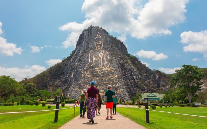 Visitors walking towards Buddha Mountain, Khao Chi Chan, with a golden Buddha engraving, near Pattaya, Thailand.