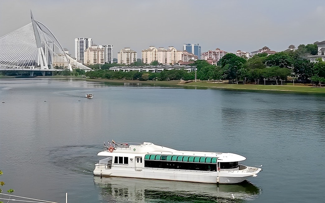 Cruise boat on Tasik Putrajaya with city skyline and bridge in the background.