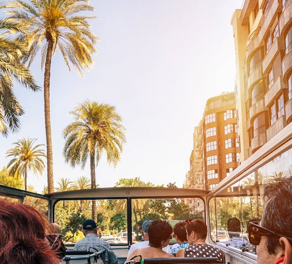 Open-top bus tour in Berlin with passengers viewing cityscape and palm trees.